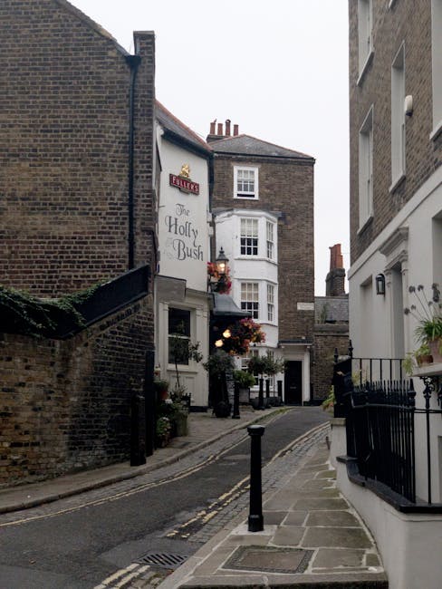 A three-story red brick building with a distinctive curved gable roof and multiple white-framed sash windows, located on a street corner with a bakery, café, and patisserie on the ground floor. The b